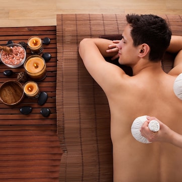 A person receiving a massage with candles and stones on a wooden floor.