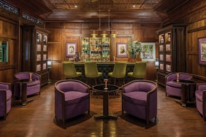 A bar area with wooden paneling, green bar stools, and purple armchairs.