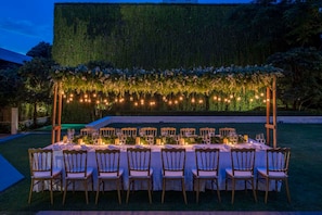An outdoor dining setup with a long table, chairs, and string lights.