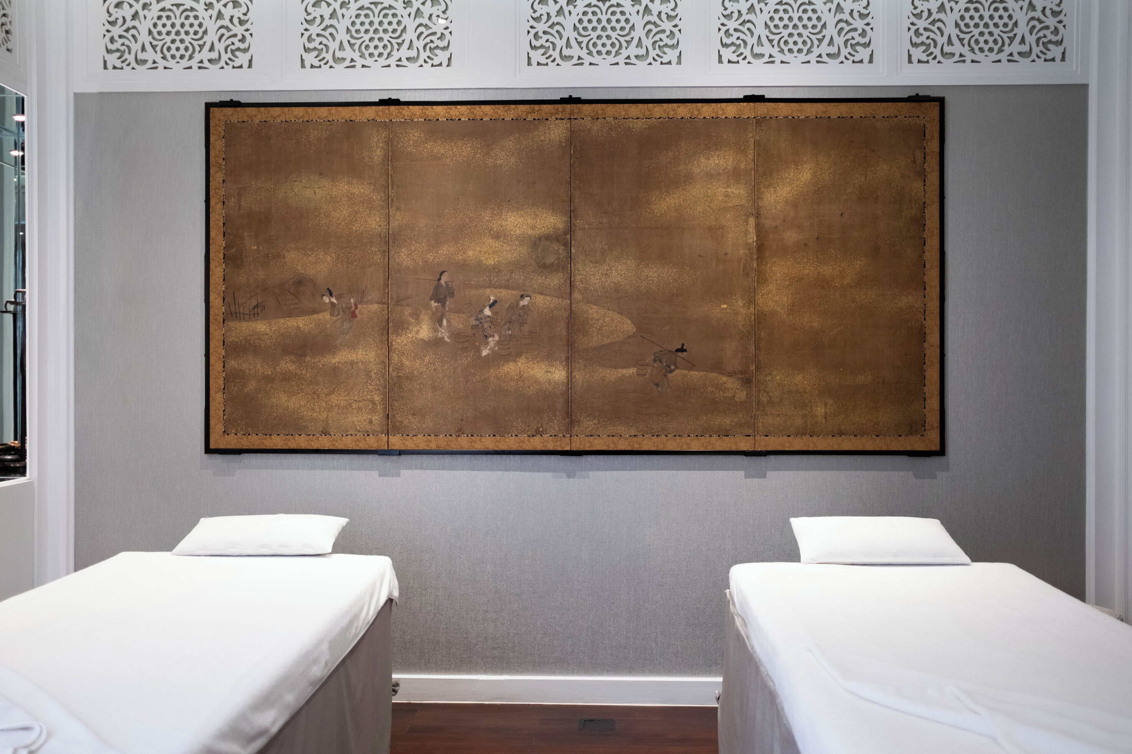 Una habitación con dos camas, una obra de arte grande en la pared y un panel decorativo blanco sobre las camas.
