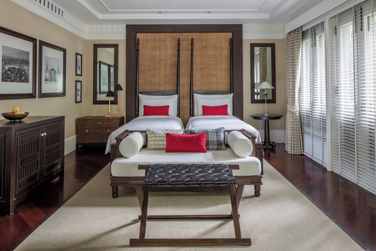 A spacious bedroom with a large bed, a bedside table, a bench, and a dresser.