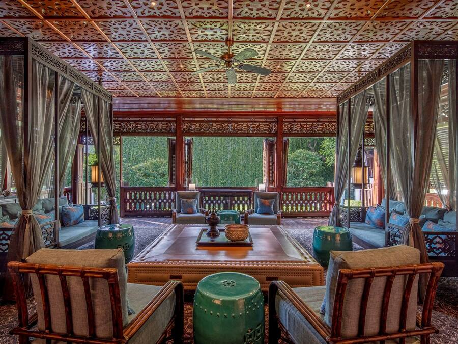 A traditional room with a wooden ceiling, a central seating area with cushions, and a view of greenery outside.