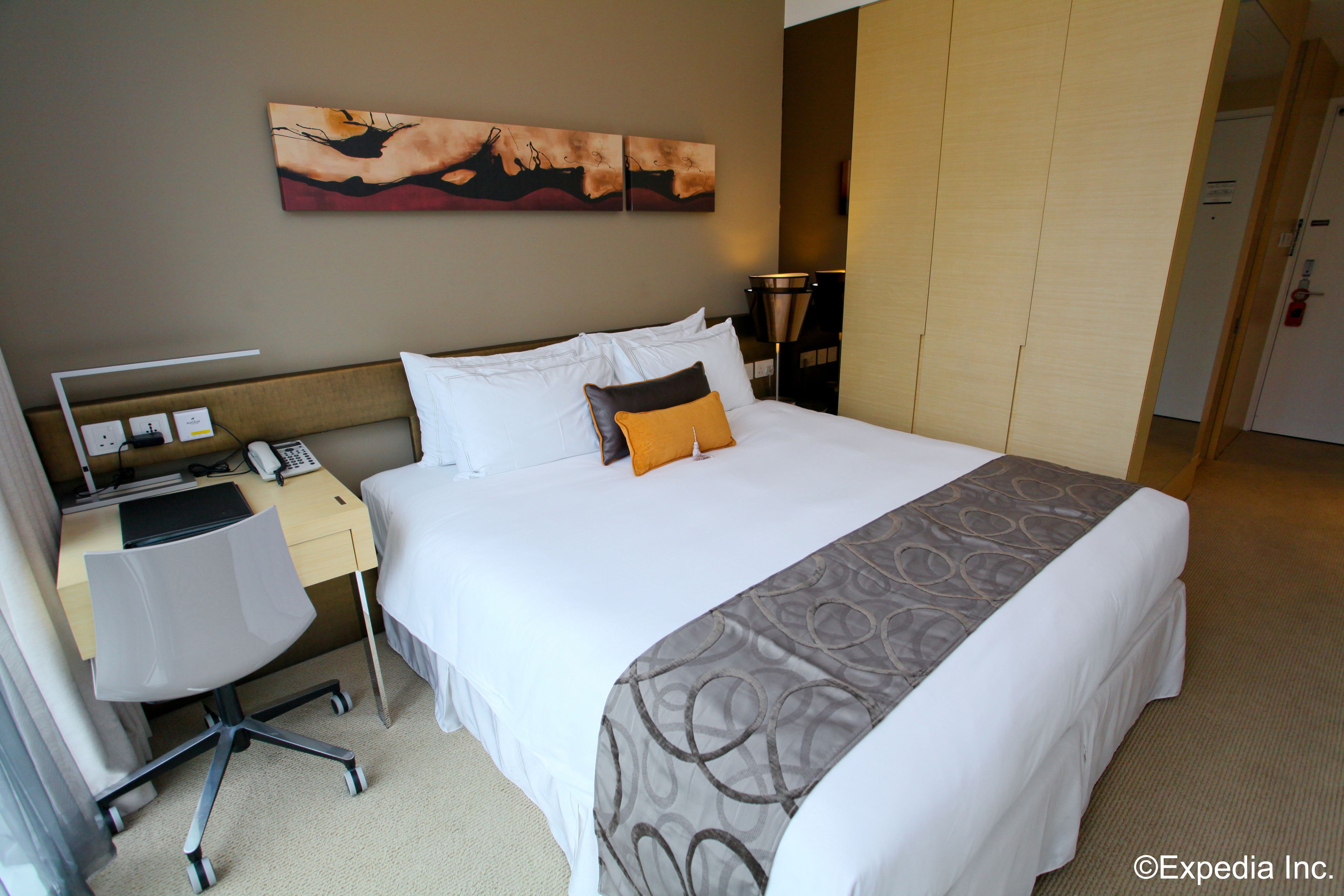 A hotel room with a bed, desk, chair, and artwork on the wall.