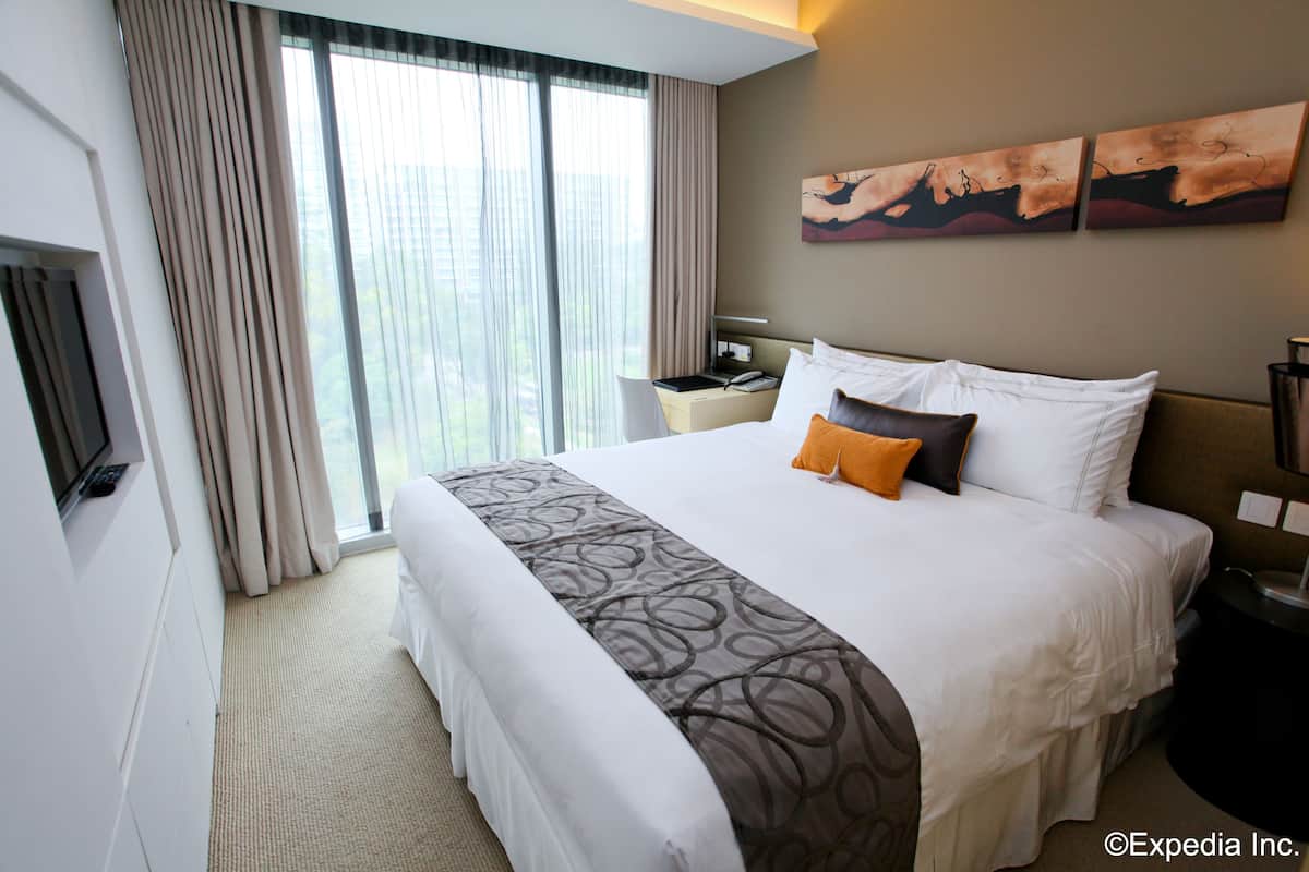 A hotel room with a large bed, a TV, a desk, and a window with curtains.