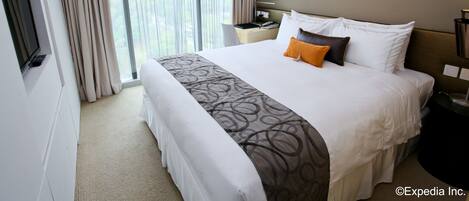 A hotel room with a large bed, a TV, a desk, and a window with curtains.