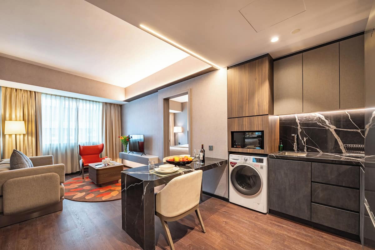 A modern hotel room with a living area, dining space, and a compact kitchen.