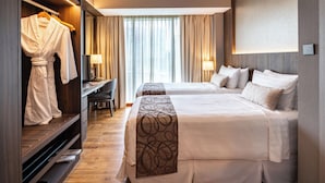 A hotel room with two beds, a desk, a robe rack, and a view of the city through large windows. - Park Avenue Rochester (Singapore)