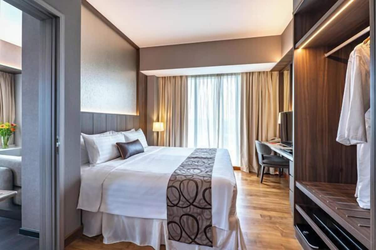 A hotel room with a bed, a desk, a chair, a wardrobe, and a TV.