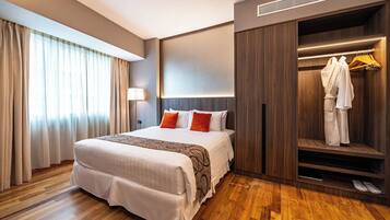 A hotel room with a large bed, a wardrobe with hanging clothes, and a shoe shelf.