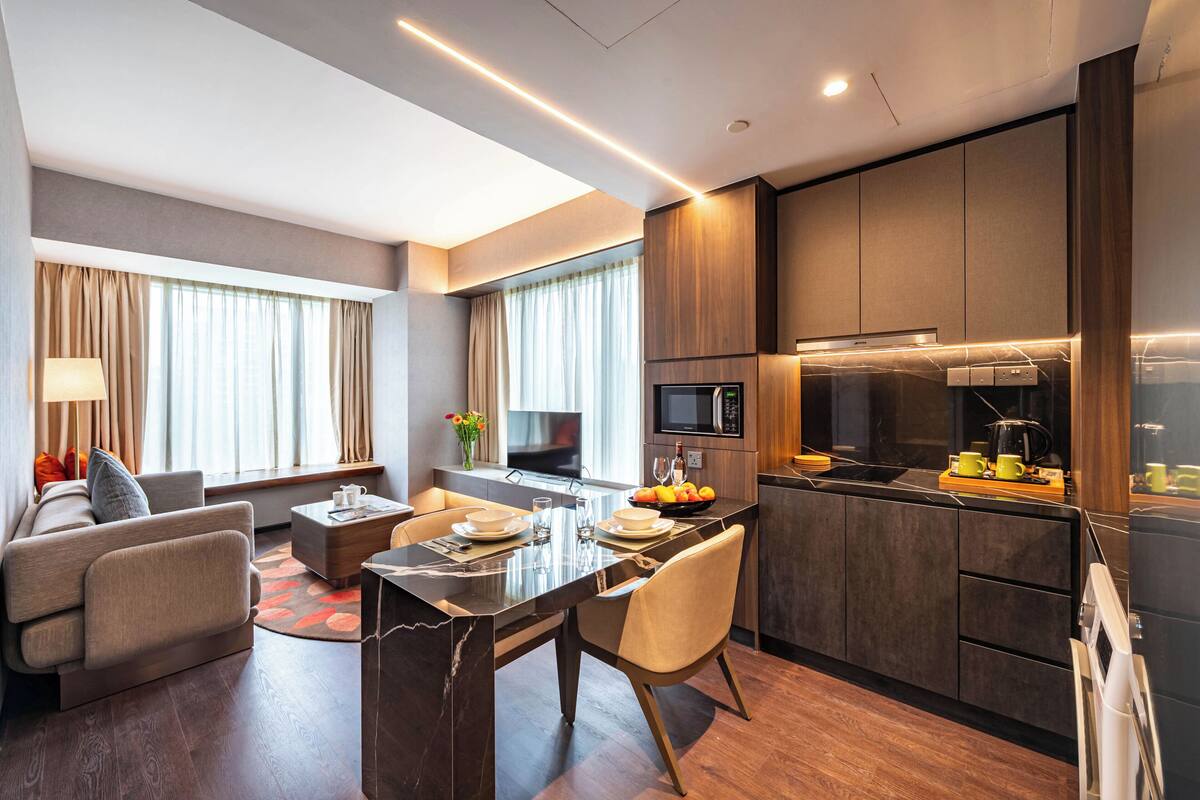 A modern hotel room with a dining area, kitchenette, and a sofa.