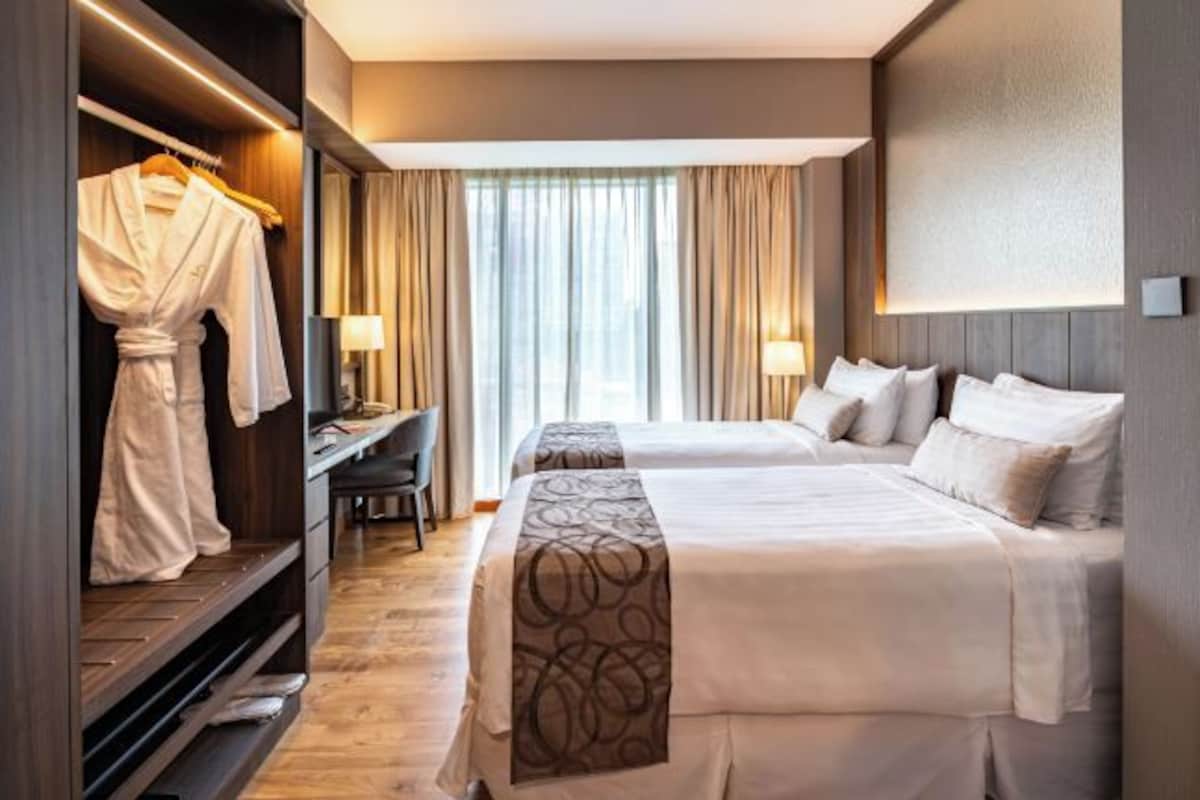 A hotel room with two beds, a desk, a wardrobe, and a view of the outdoors.