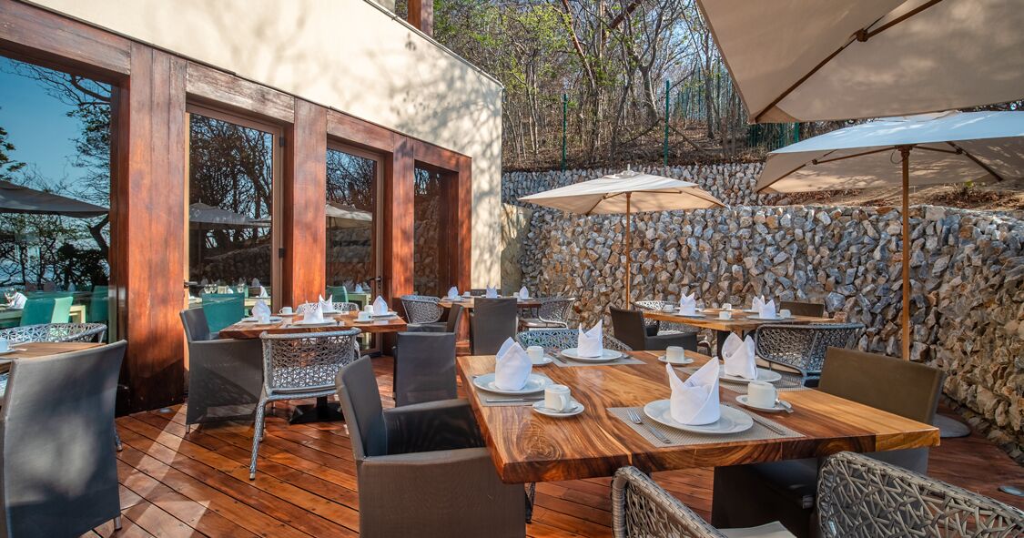 Un espace de restauration en plein air avec des tables et des chaises en bois, des murs en pierre et des parasols.