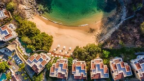 Vista aérea de un resort costero con villas frente a la playa, una playa de arena y un acantilado rocoso.