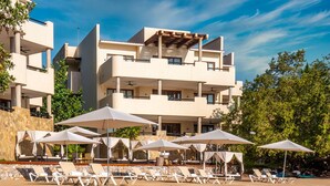 Un hotel moderno con varios balcones, mobiliario exterior con sombrillas y una zona de piscina.
