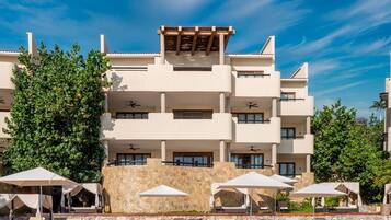 Un hôtel à plusieurs étages, doté d’une façade en pierre, d’une terrasse avec des parasols et surplombant un ciel d’un bleu éclatant.