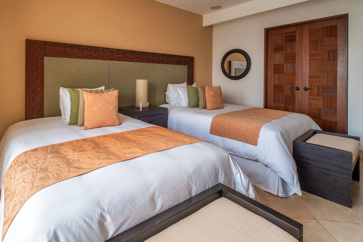 A hotel room with two beds, a nightstand, a mirror, and a wardrobe.