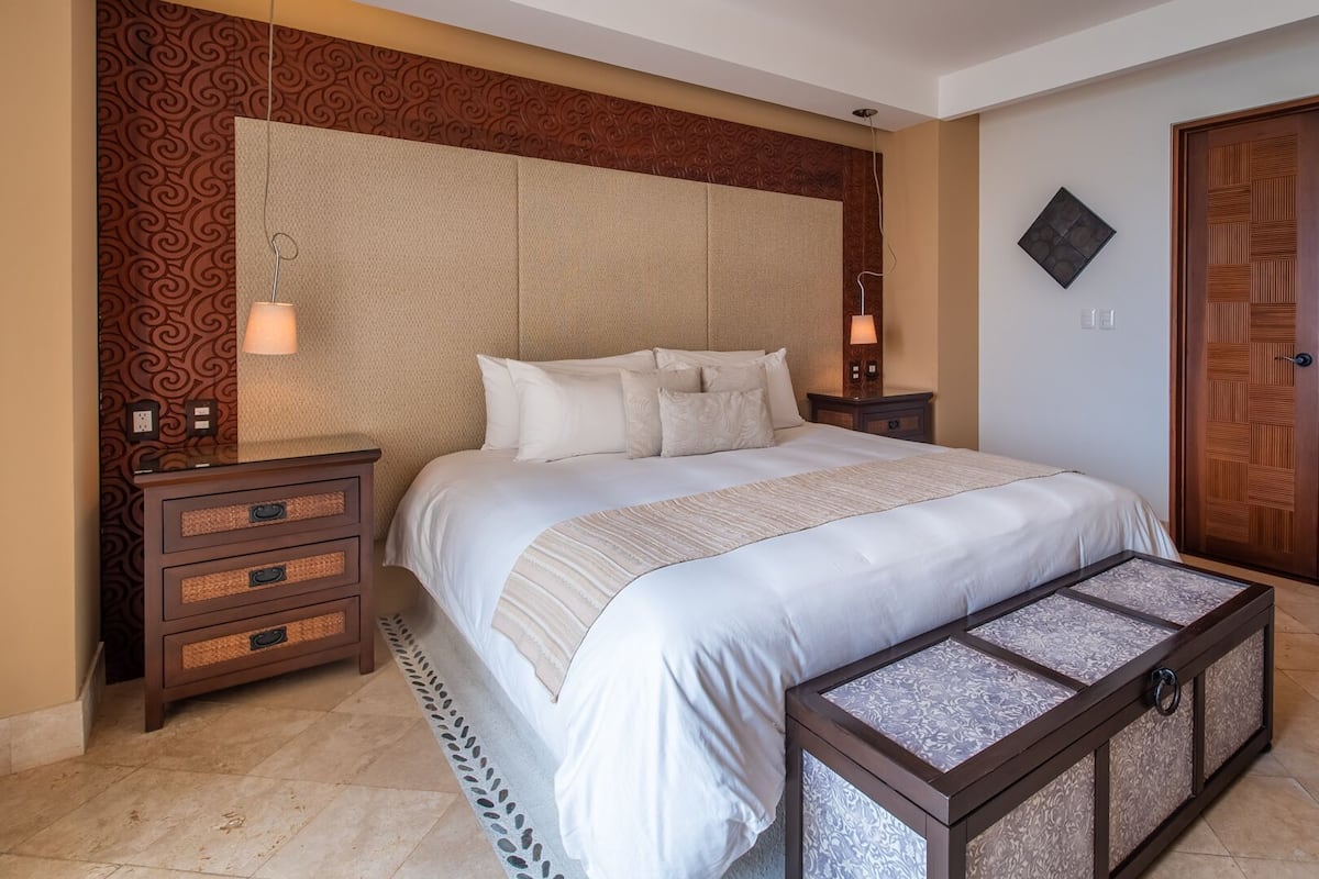 A neatly arranged bedroom with a large bed, two bedside tables, a nightstand, a bench, and a wooden wardrobe.