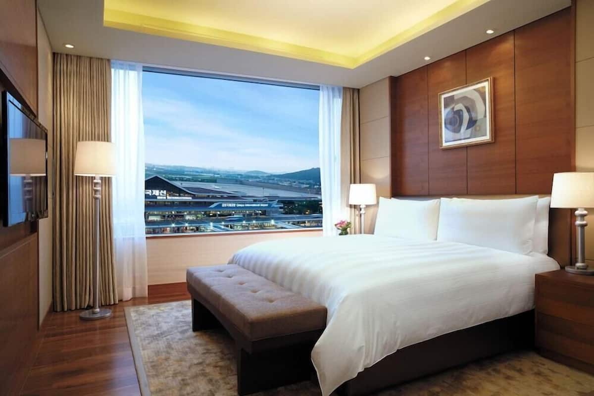 Une chambre d’hôtel avec un grand lit, un banc, une télévision et une vue sur le paysage urbain.