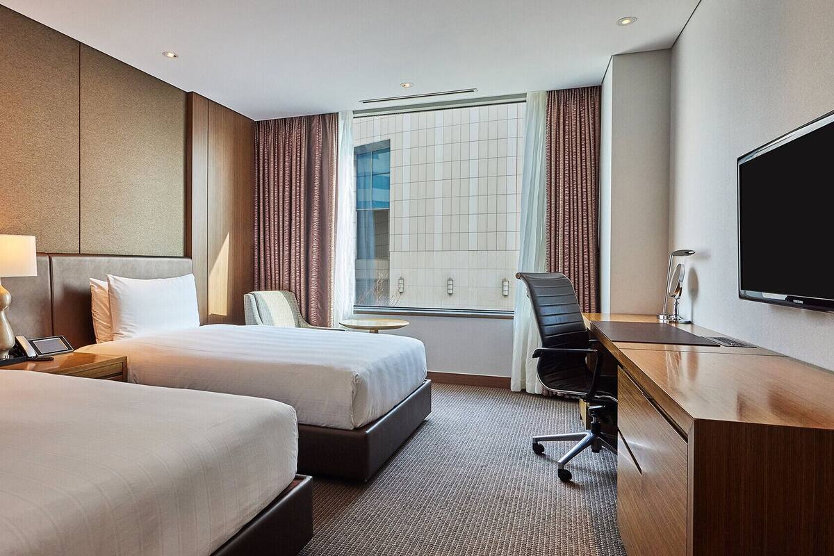Une chambre d’hôtel avec deux lits, un bureau avec une chaise, une télévision et une fenêtre avec des rideaux.