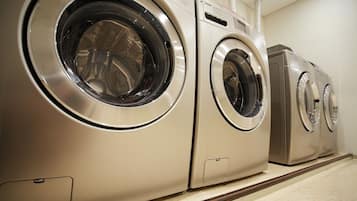 A row of stainless steel front-loading washers in a commercial setting.