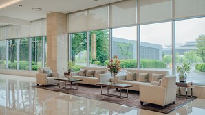 Een ruime lobby met grote ramen, een zithoek met banken en salontafels, en een schoon, modern design.