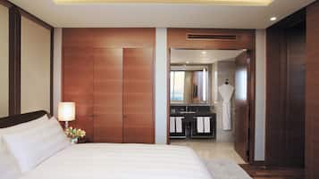 Habitación de hotel con una cama grande, una mesita de noche con lámpara, un armario de madera, baño con lavabo y espejo, y una bata colgada en la puerta.