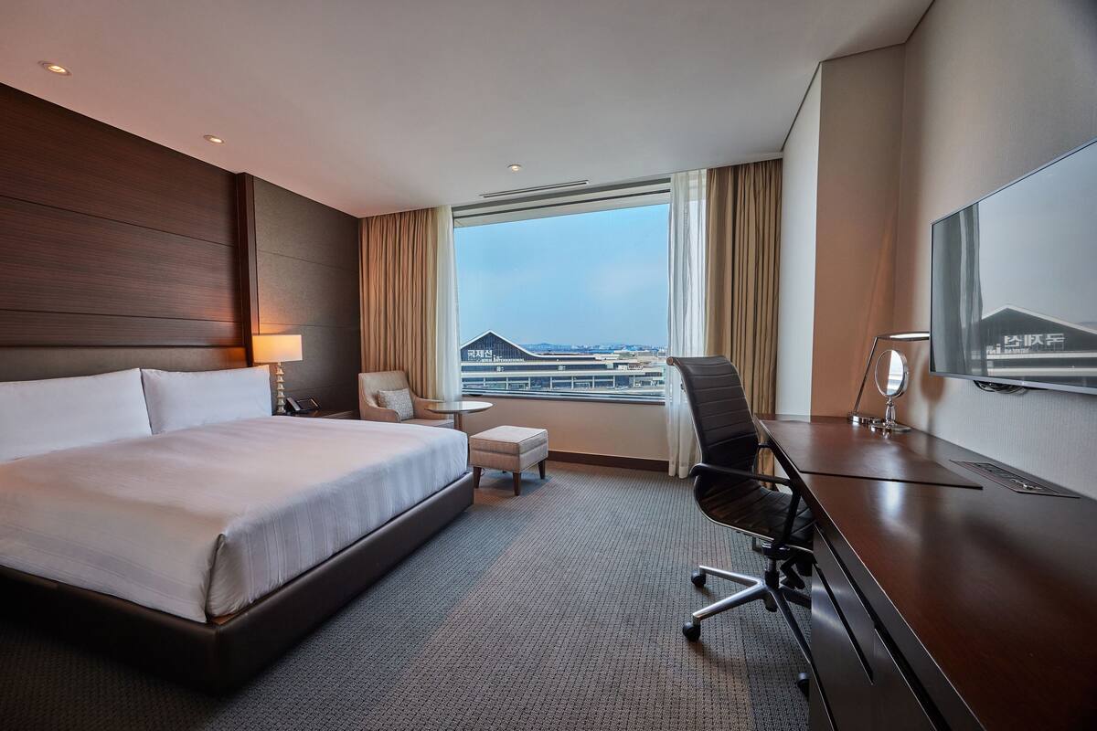 Une chambre d’hôtel avec un grand lit, un bureau, une chaise, une petite table et un téléviseur.