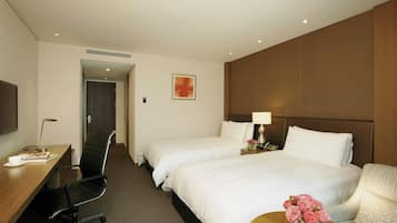 Habitación de hotel con dos camas, un escritorio con silla, televisión y una mesita con un jarrón de flores.