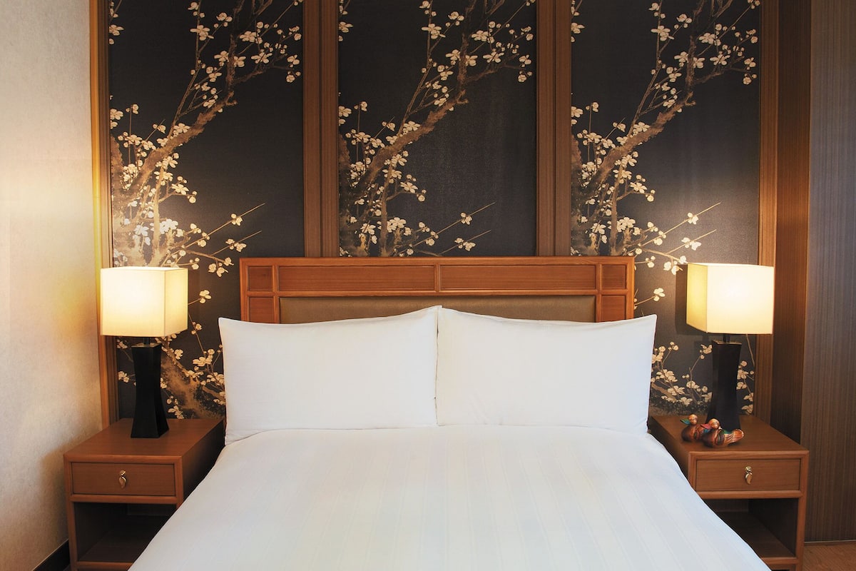 A hotel room with a large bed, two bedside tables with lamps, and a wall with a floral mural.