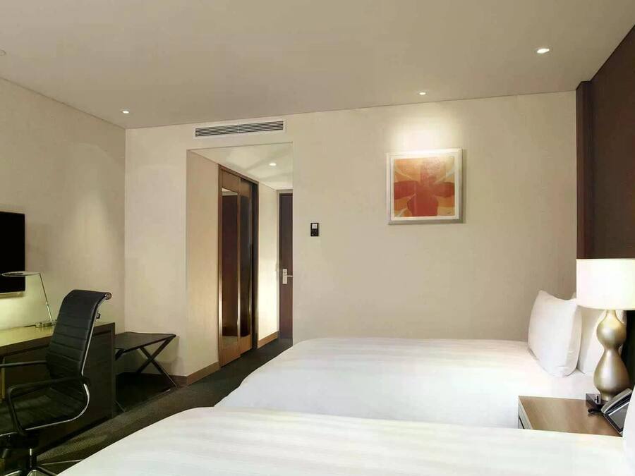 A hotel room with a bed, a desk with a chair, a TV, and a painting on the wall.