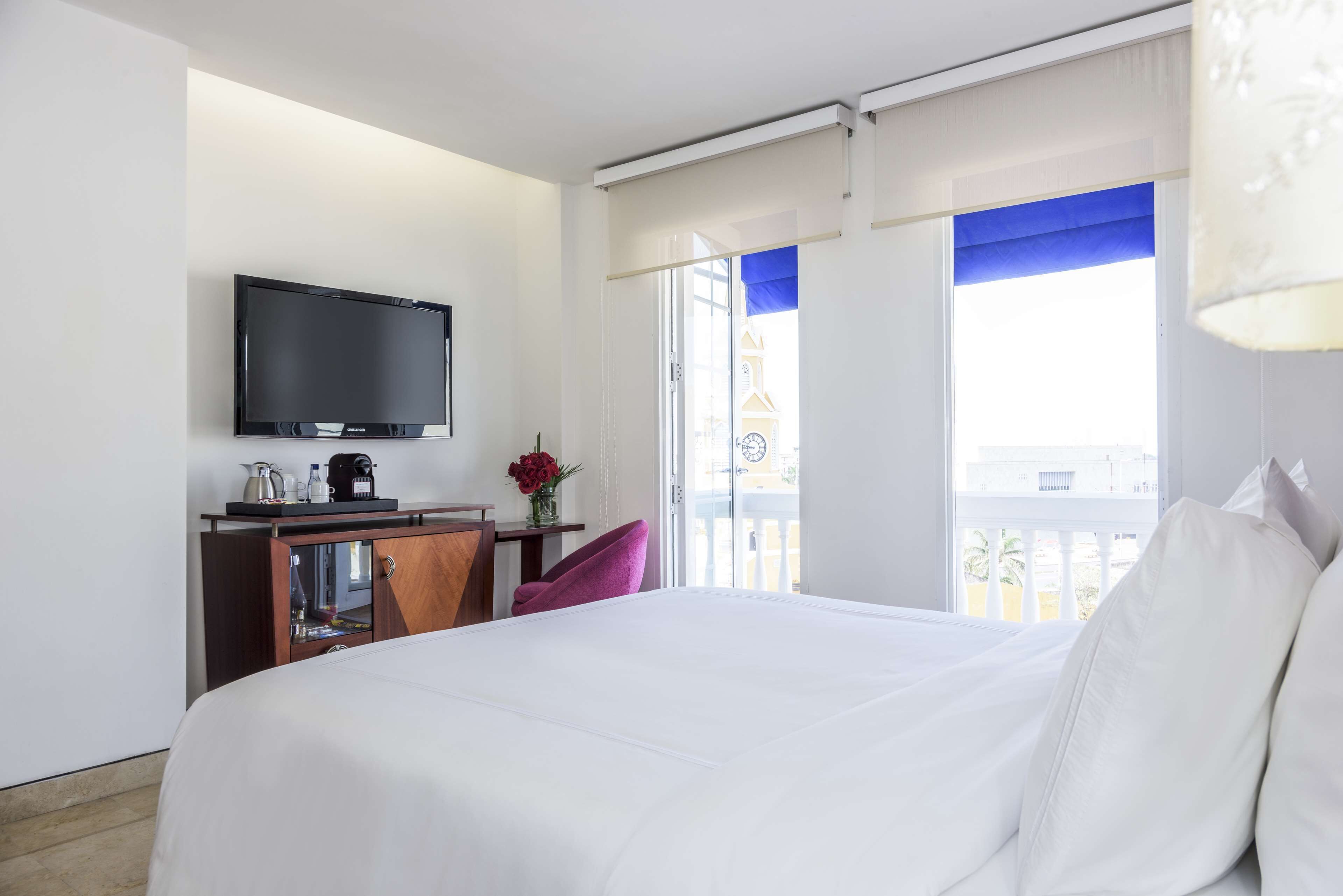 Habitación de hotel con cama, escritorio con televisor, una silla y vista a un edificio por la ventana.