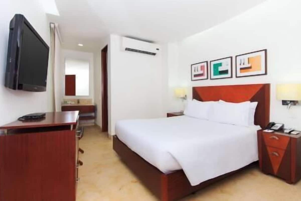 A hotel room with a bed, a desk, a TV, and a mirror.