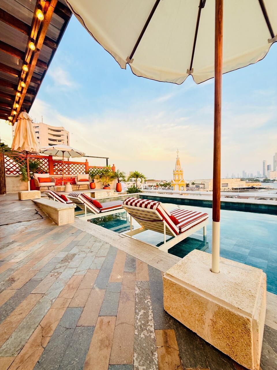 A rooftop pool area with lounge chairs, a pool, and a view of a cityscape including a clock tower.