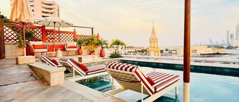 A rooftop pool area with lounge chairs, a pool, and a view of a cityscape including a clock tower.