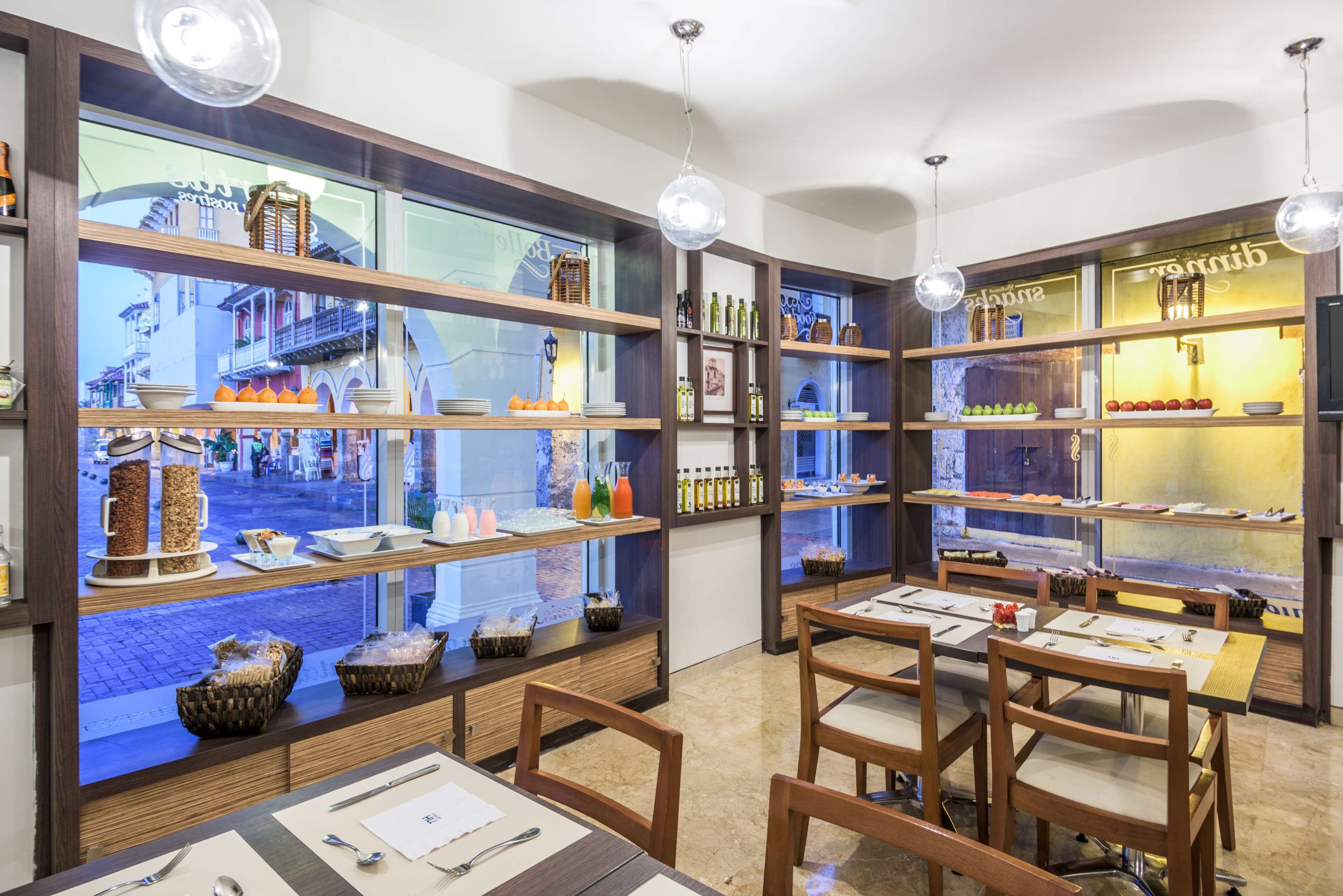 Ein Restaurant mit Holzböden, auf denen Speisen und Getränke präsentiert werden, Tische mit Besteck und hängenden Pendelleuchten.