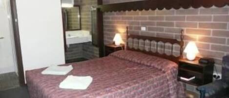 A bedroom with a brick wall, a bed with a patterned bedspread, two bedside lamps, and a nightstand with a lamp.