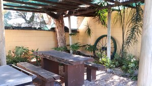 Un banco de madera bajo una pérgola, rodeado de plantas en macetas y un gran carrusel.