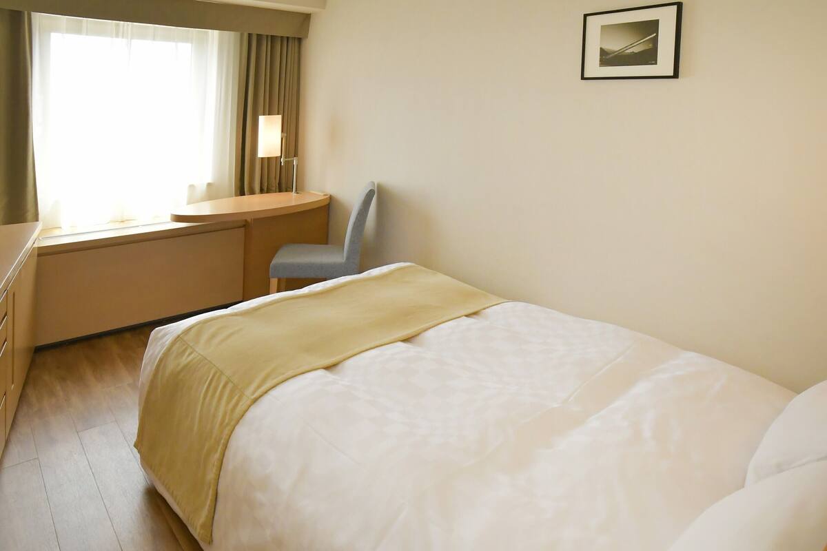 A hotel room with a bed, a desk, a chair, and a window with curtains.