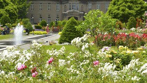 A large building with a symmetrical facade, a central entrance, and a fountain in the foreground.