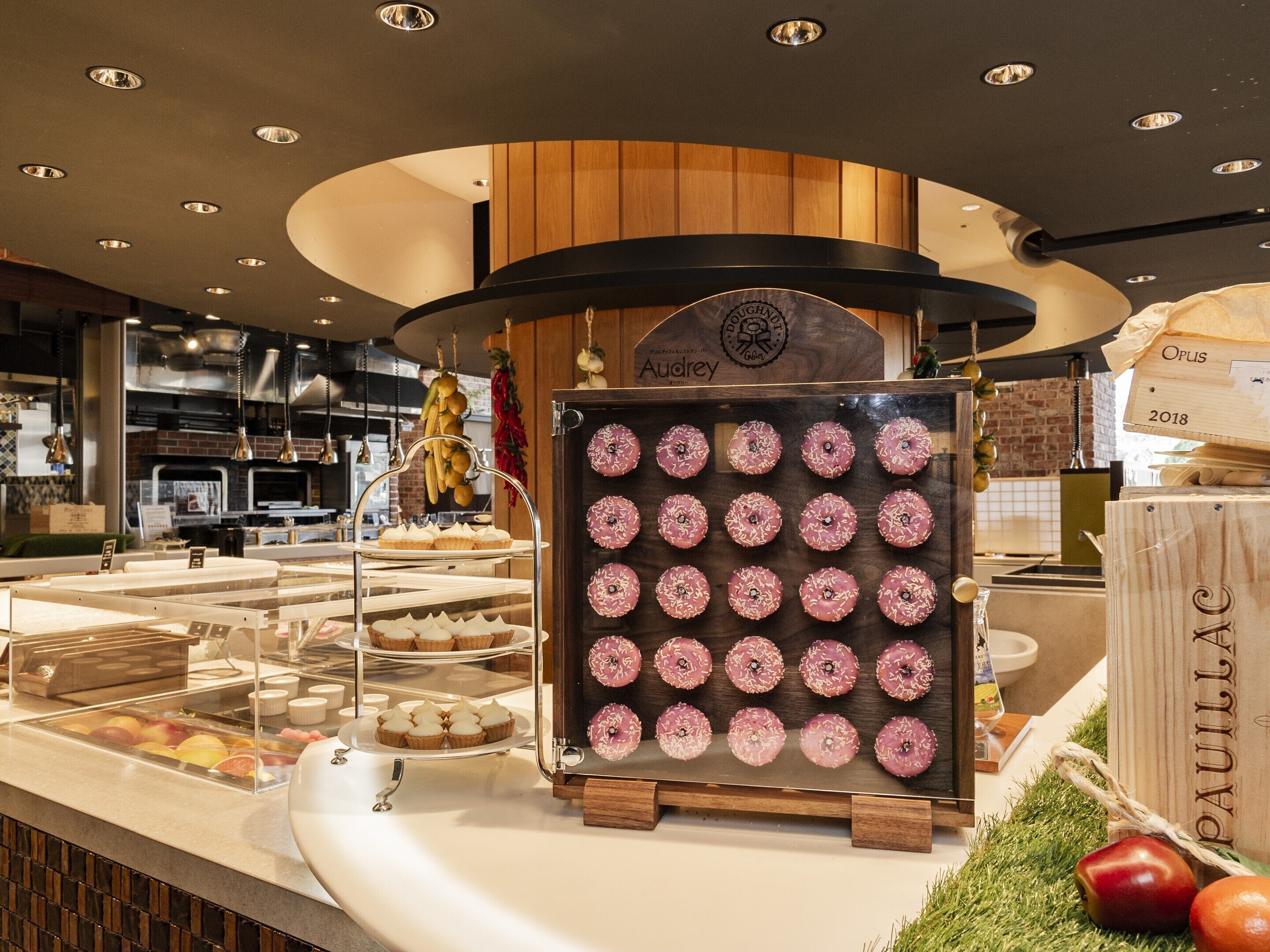 A bakery display with donuts and pastries, a wooden sign with the name "Audrey," and a sign indicating "Opus 2018."