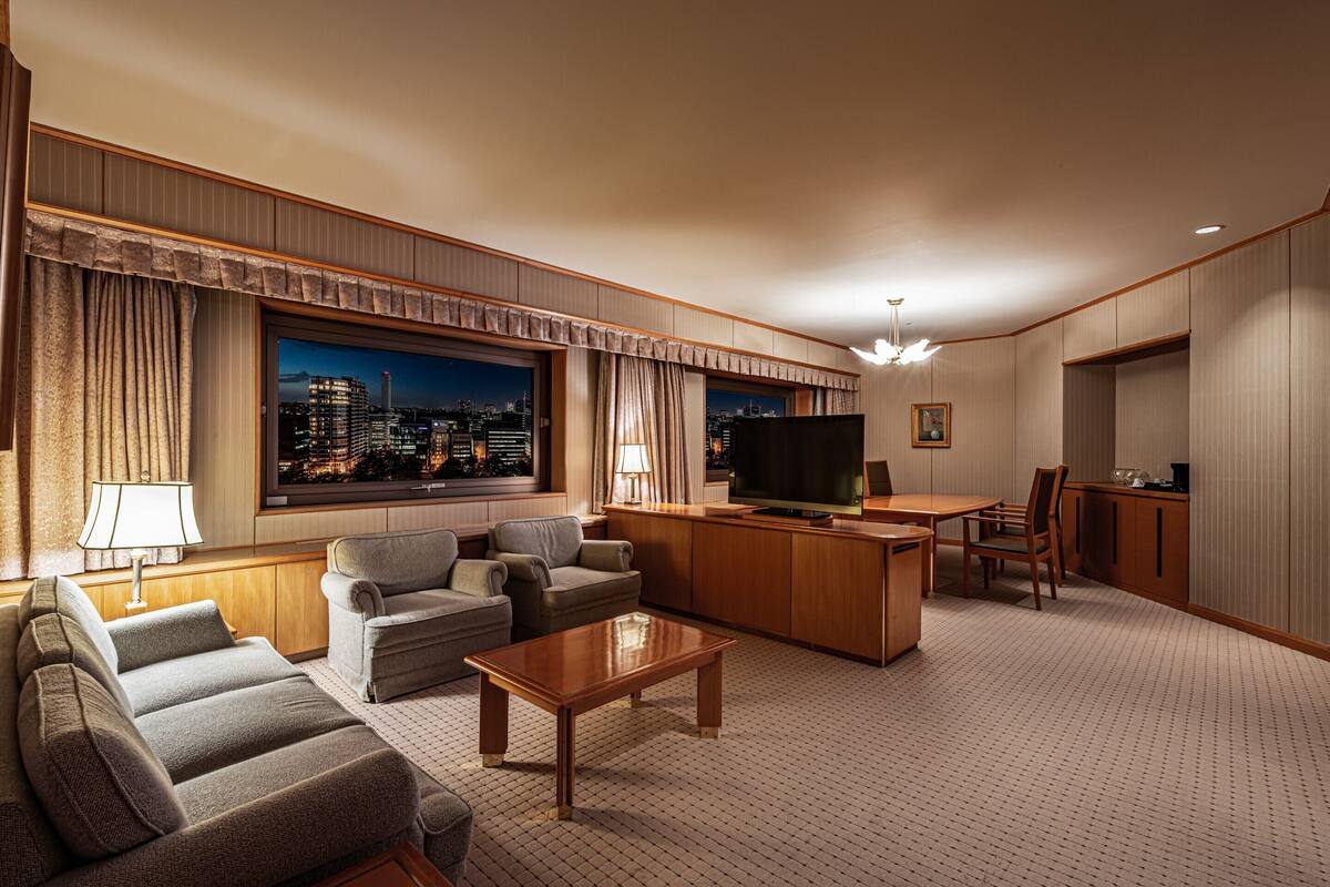 A hotel room with a seating area, a television, a desk, and a city view.