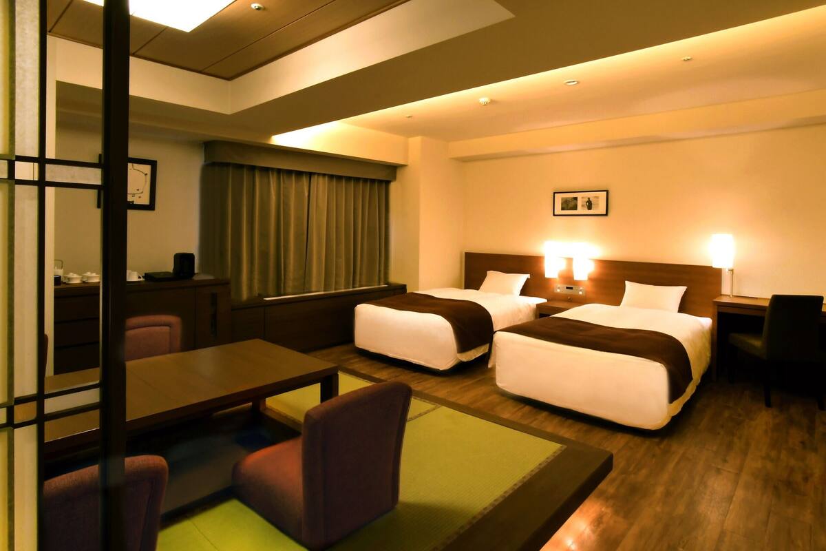 A hotel room with two beds, a desk, a chair, a small table, and a sofa.