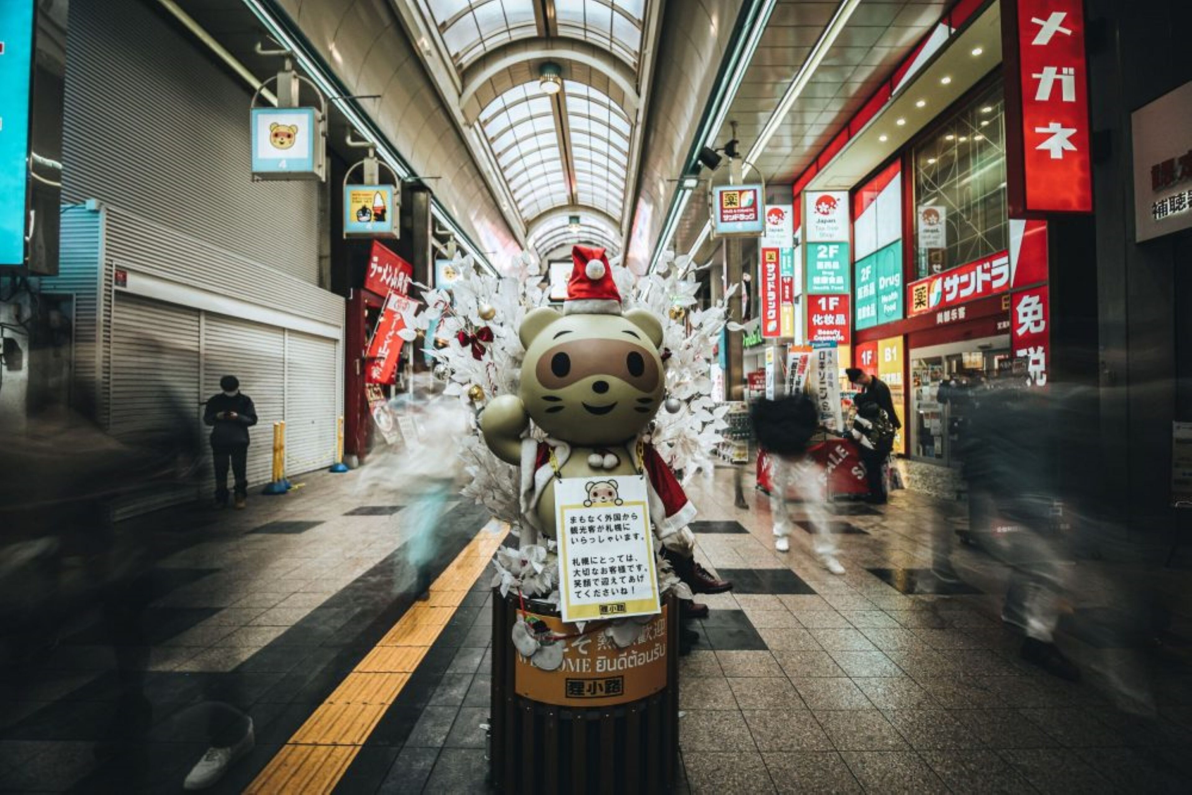 A shopping mall with a large teddy bear decoration in the center, surrounded by various signs and advertisements.