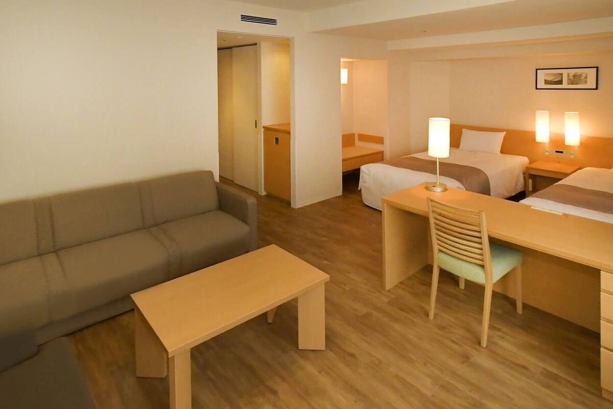 A hotel room with a sofa, a desk, a chair, and two beds.
