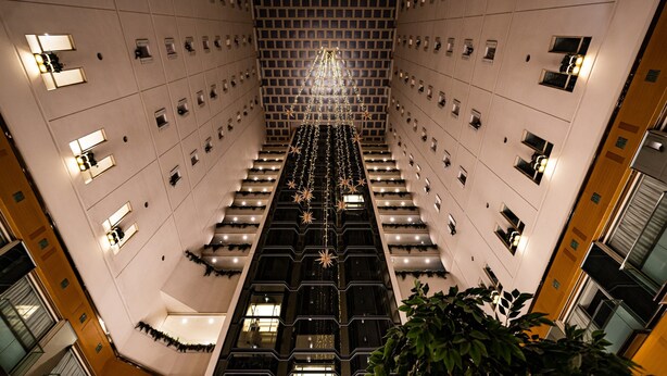 A modern hotel interior with a central staircase, multiple floors, and a decorative light fixture at the top.