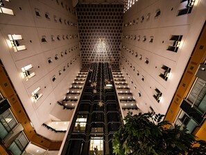 Interior moderno de un hotel con una escalera central, varios pisos y un elemento decorativo de iluminación en la parte superior.