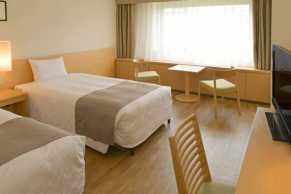 A hotel room with two beds, a desk, a chair, and a TV.