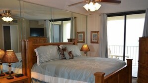 A bedroom with a large bed, wooden headboard, bedside lamps, a mirror, and a view of the balcony. - Sunswept Condominiums (Orange Beach)