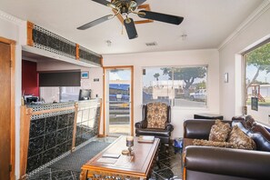 A room with a ceiling fan, a dining table with chairs, a leather sofa, and a large window with a view of the outside. - Carlsbad Inn New Mexico (Carlsbad)