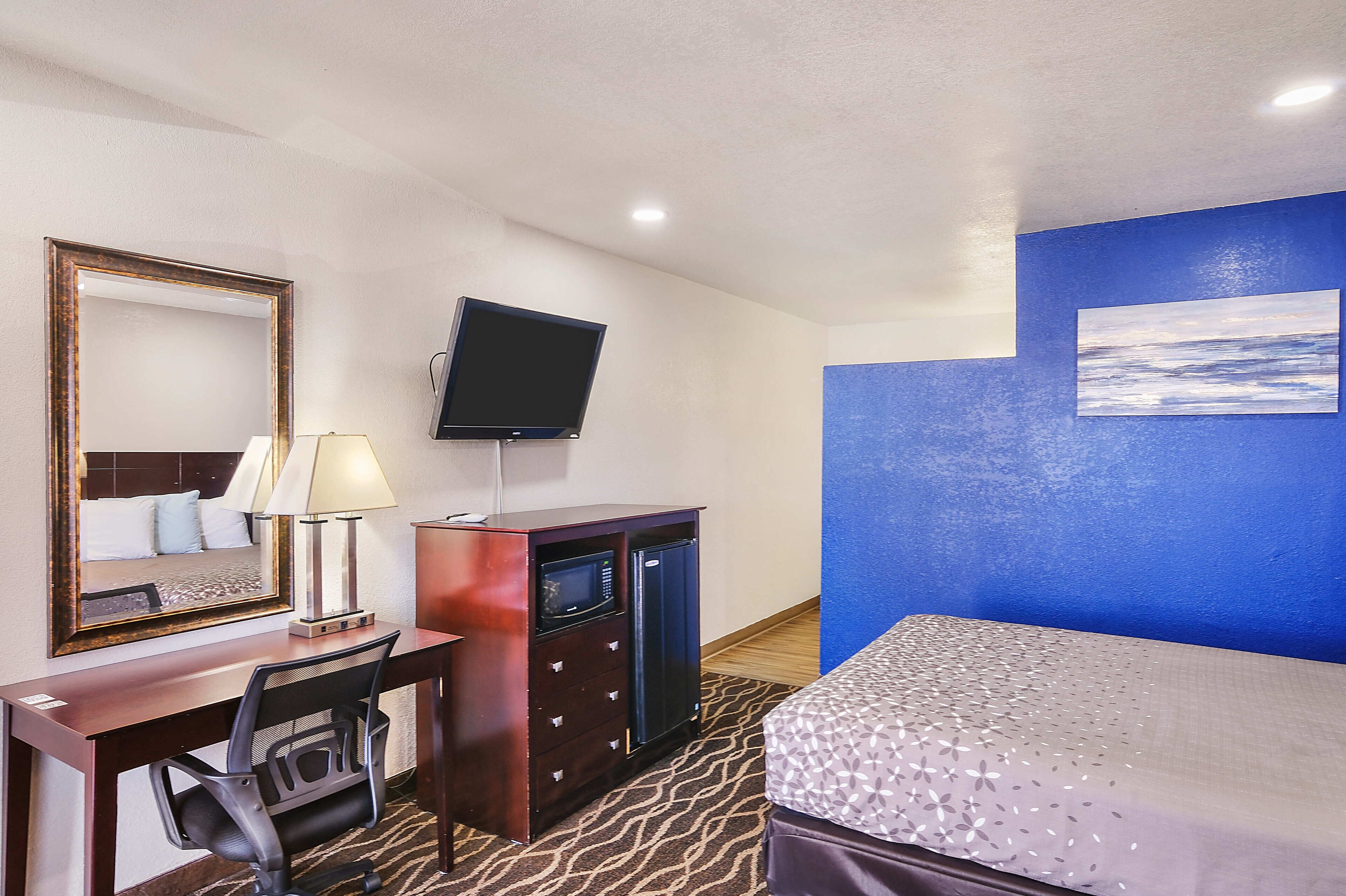A hotel room with a bed, a desk with a lamp, a television, a dresser, and a mirror.